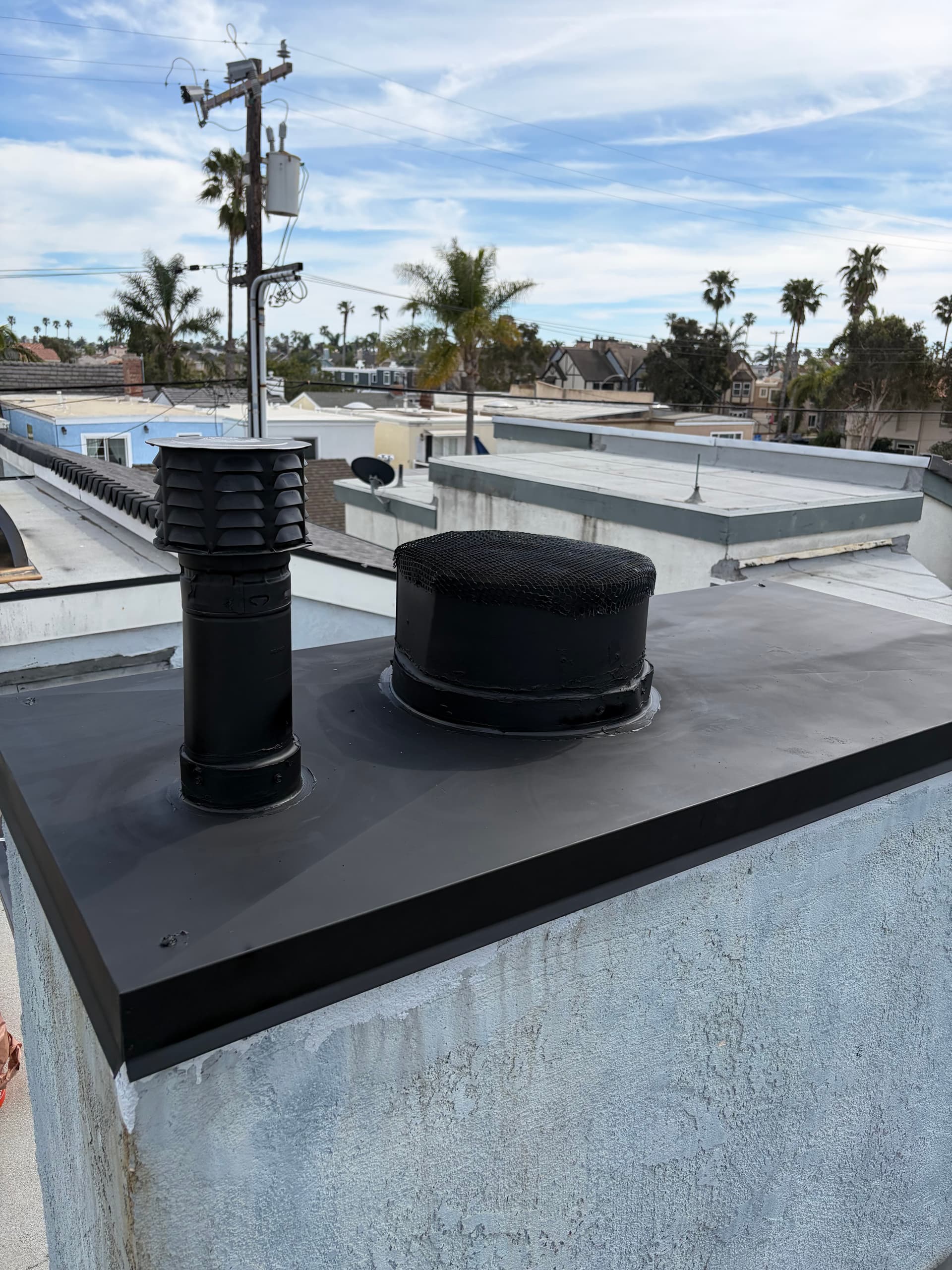 Black steel chimney cap with dual flue pipes on a stucco home