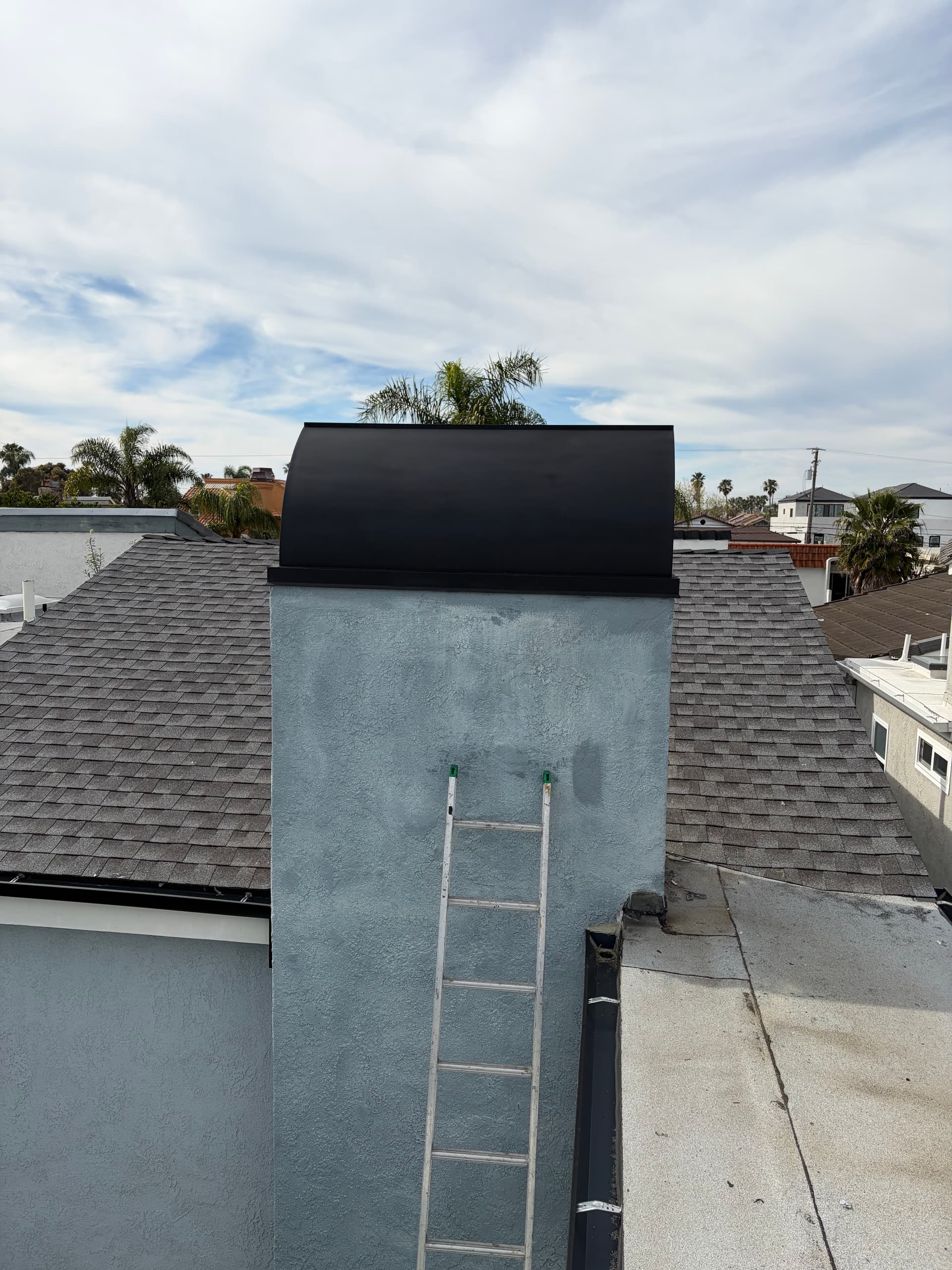 Black chimney shroud side profile on a stucco chimney with shingle roof