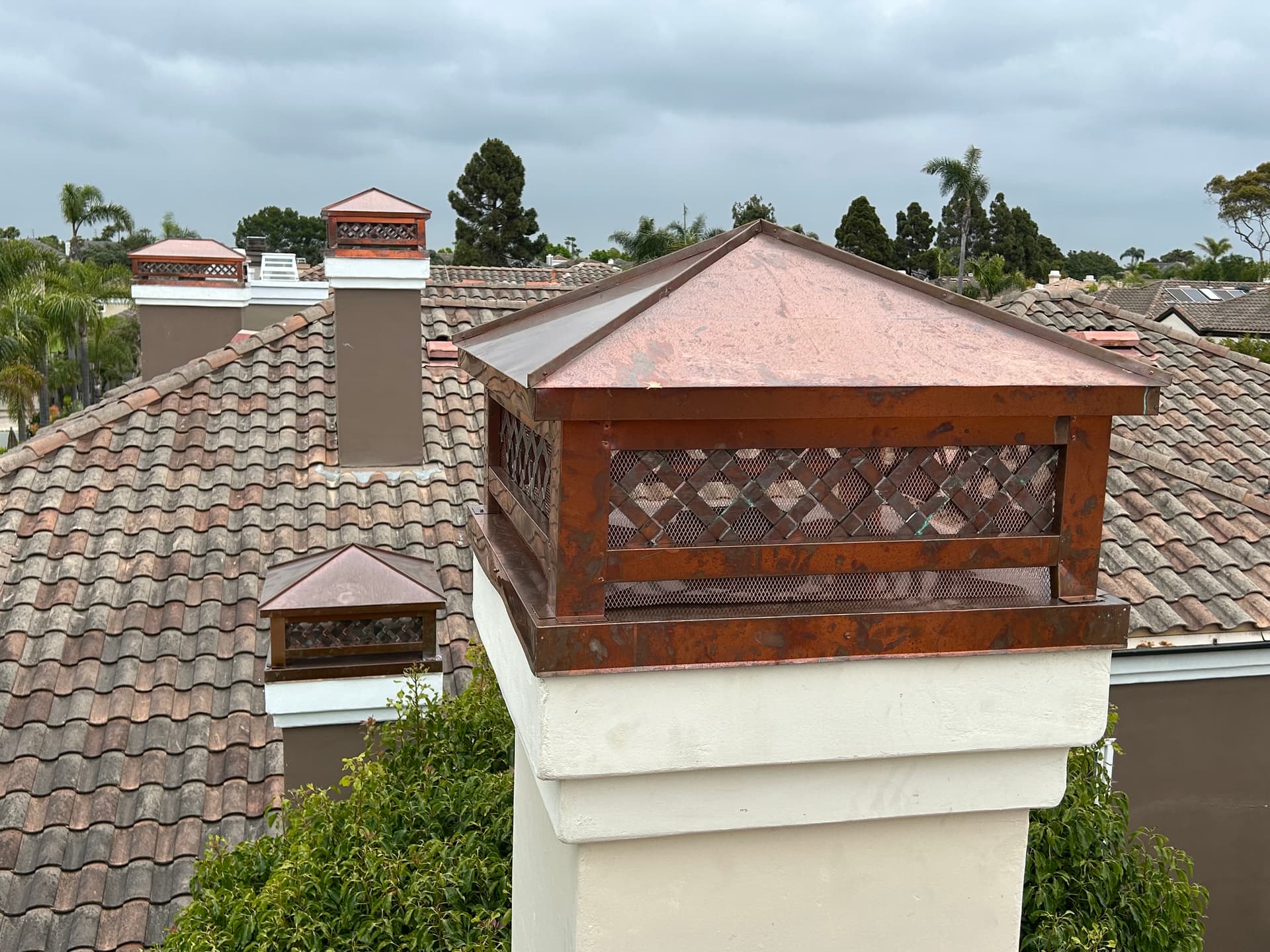 Copper chimney cap with lattice spark arrestor mesh showing natural patina
