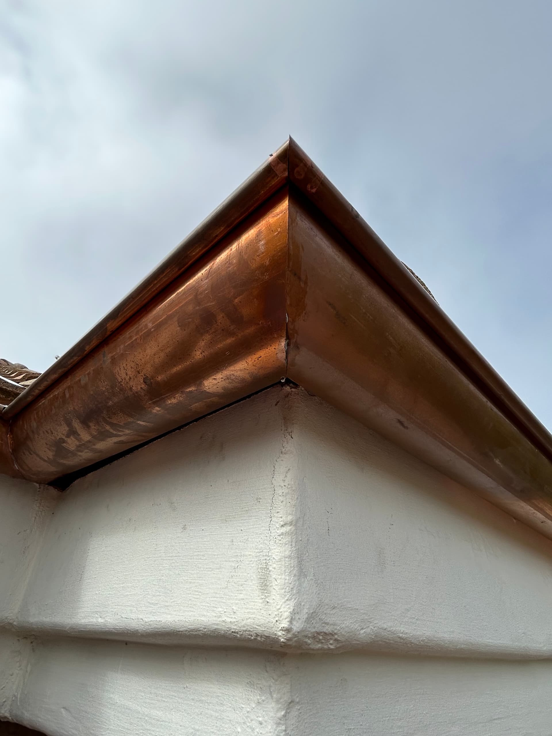 Close-up of copper angle face gutter miter joint on stucco home