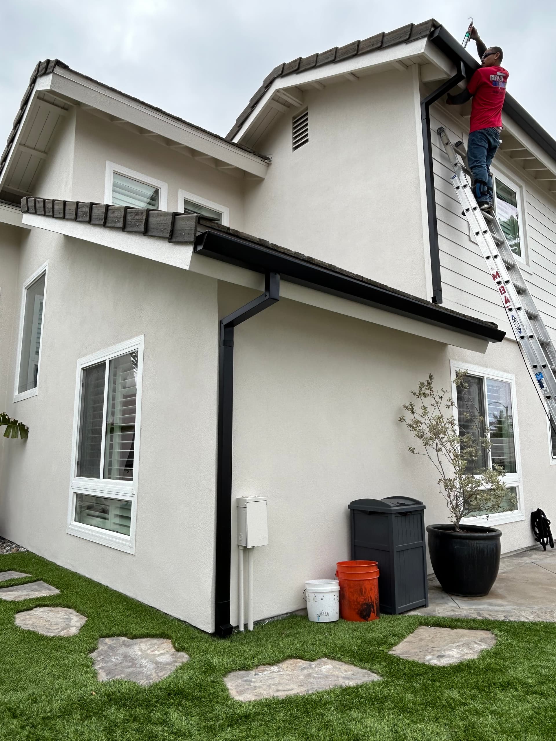 Seamless gutter installation in progress on a two-story stucco home with crew on ladder