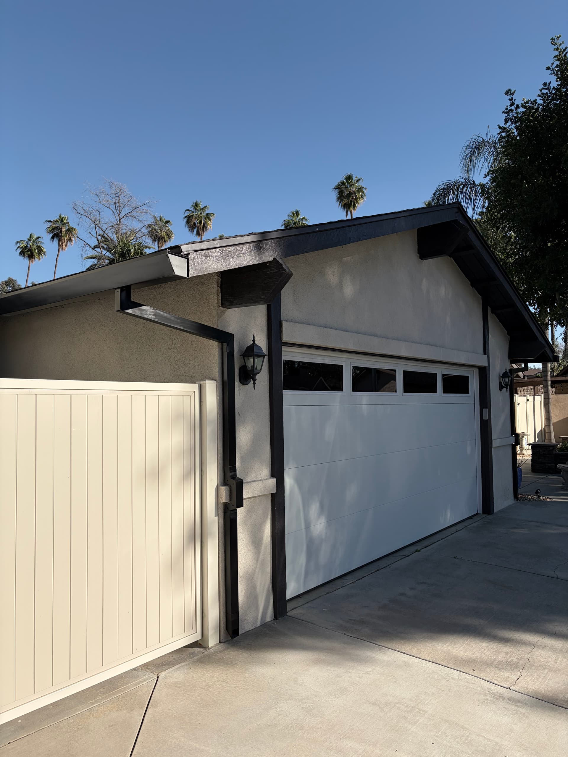 Black seamless gutter and downspout on a modern two-story stucco home with palm trees